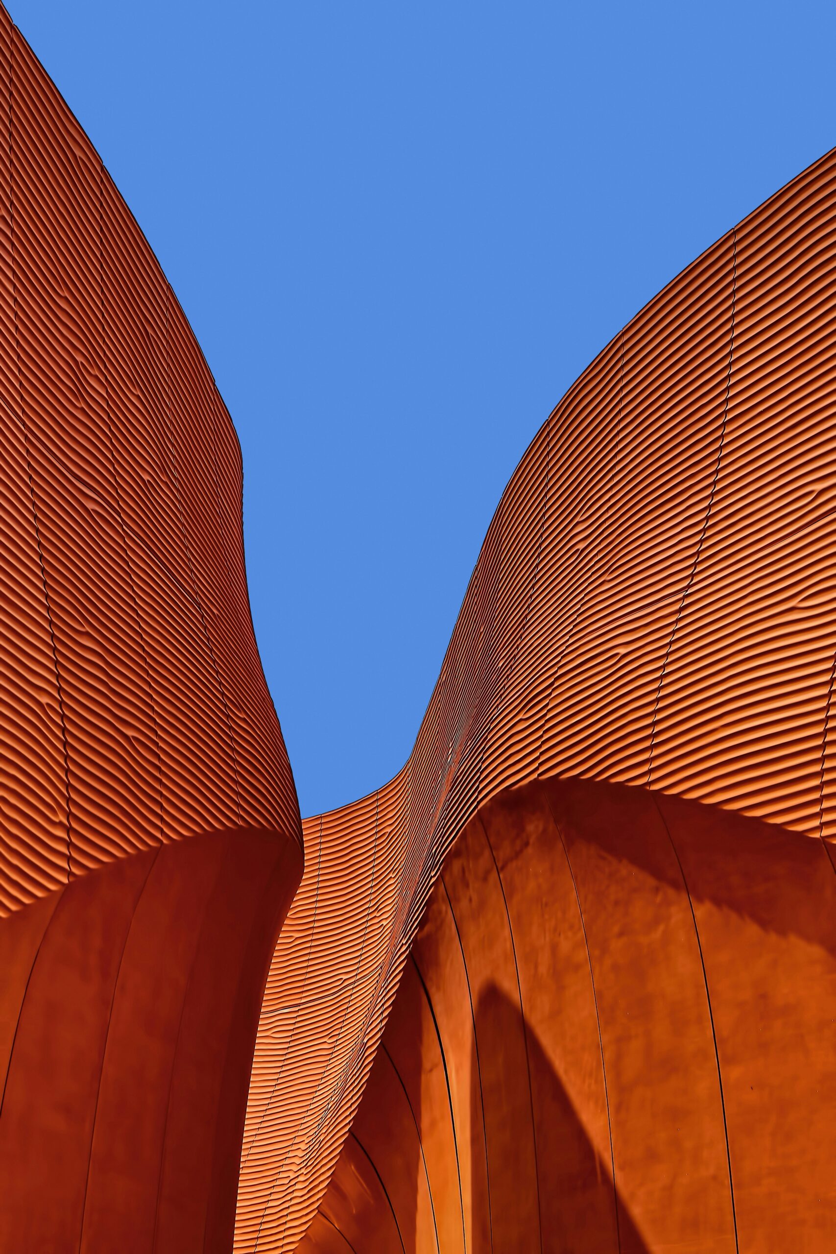 Futuristic architecture featuring wavy, orange textured walls under a clear blue sky.